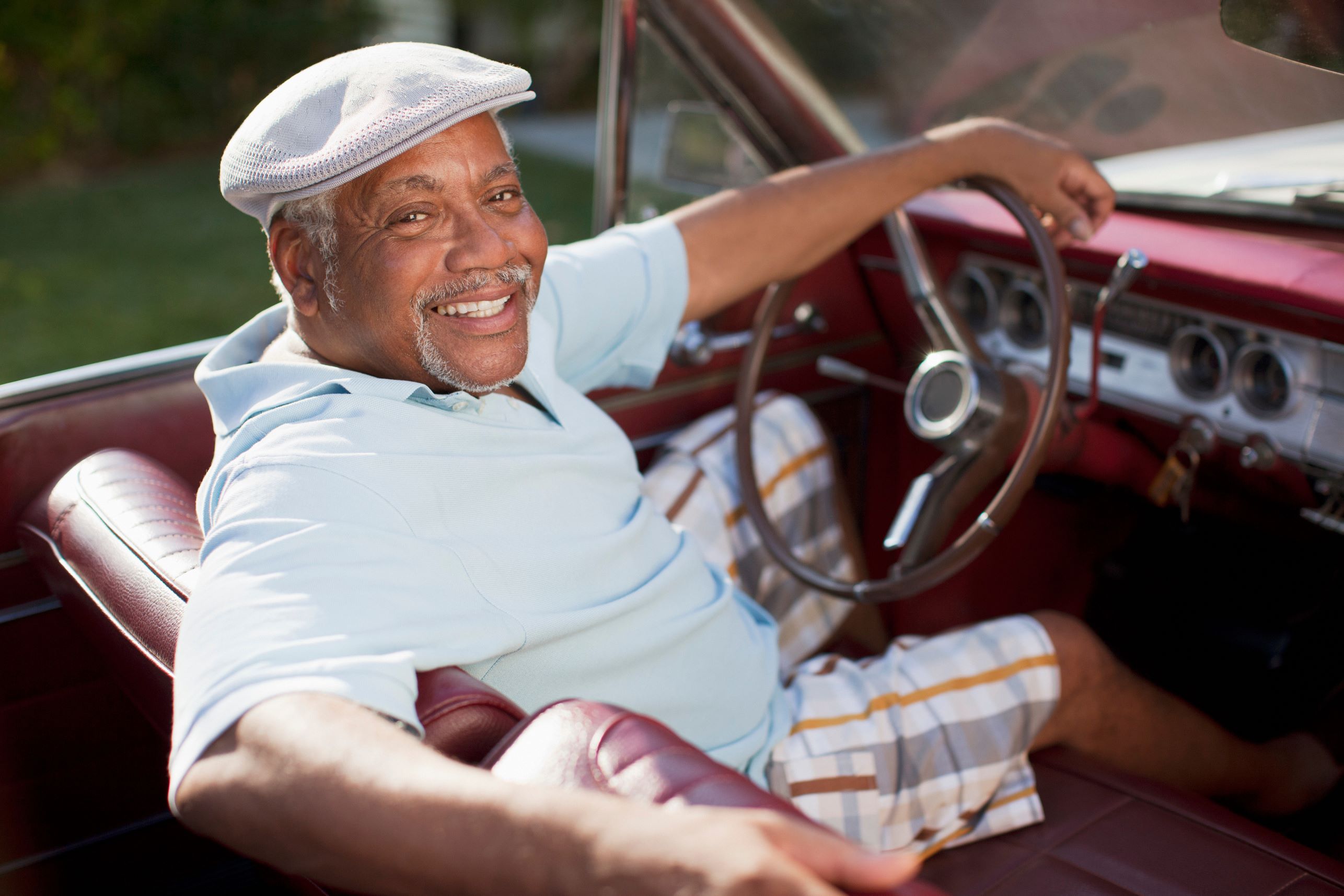 Smiling older man in the driver's seat of a red convertible.